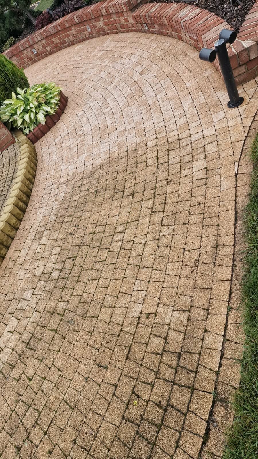 Kaskadowo ułożona kostka brukowa w odcieniach beżu, tworząca ścieżkę ogrodową z elementami zieleni i oświetleniem. Widok z góry, podkreślający wzór ułożenia.
