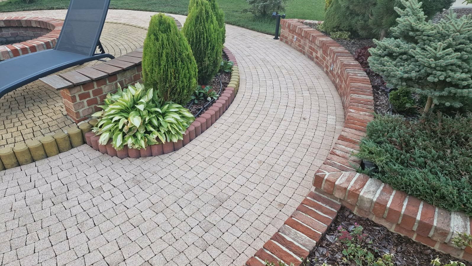 Kaskadowa ścieżka z kostki brukowej w ogrodzie, obrzeża z cegły i roślin, krzesło ogrodowe w tle, widok z góry.