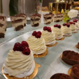 Elegancki bufet deserowy: tiramisu w szklankach, bezy z malinami i czekoladowe tartaletki na szklanym stole, idealne na wykwintny catering.