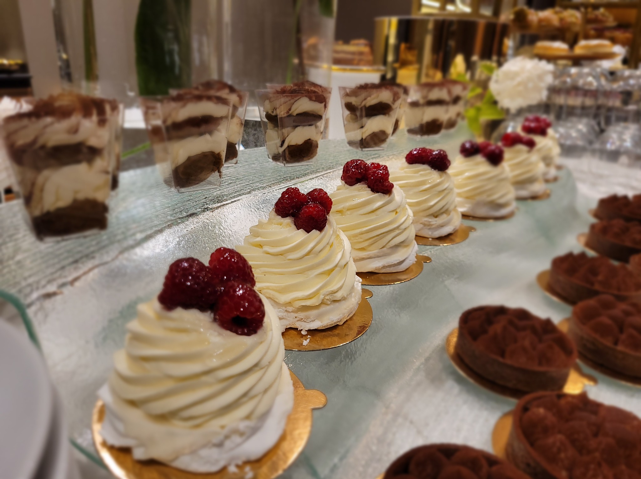 Elegancki bufet deserowy: tiramisu w szklankach, bezy z malinami i czekoladowe tartaletki na szklanym stole, idealne na wykwintny catering.