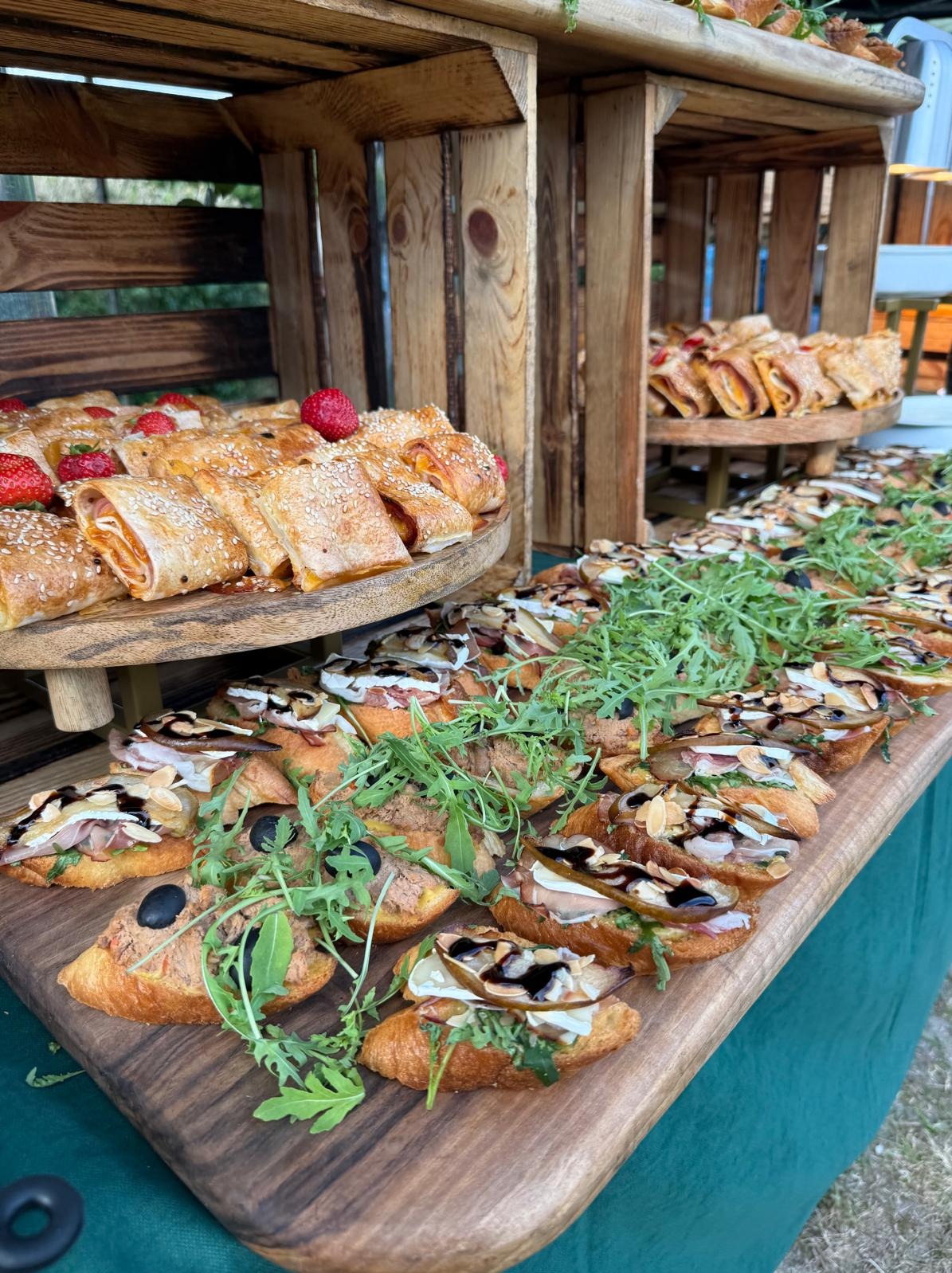 Elegancki catering: kanapki z rukolą, roladki z sezamem i truskawkami na drewnianych paterach i skrzynkach. Ujęcie z bliska, bogata ekspozycja.