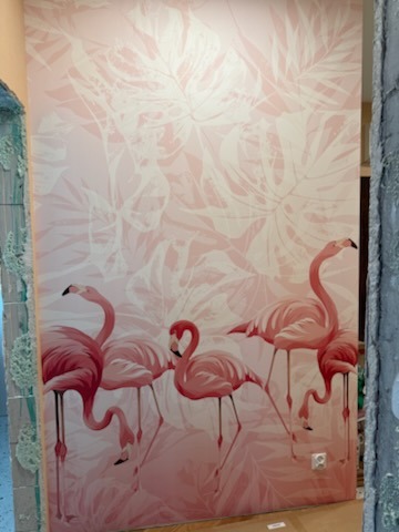 Tapeta z motywem flamingów w odcieniach różu, świeżo położona na ścianie w Łodzi. Widoczny fragment gniazdka elektrycznego i surowy fragment ściany obok.