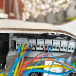 Tomasz Piecyk voltom instalacje elektryczne pomiary - Szczegółowe ujęcie podłączeń elektrycznych w szarej skrzynce sterującej, z widocznymi kolorowymi przewodami wpiętymi do złączek oznaczonych 'FLASH', 'ELS', 'BLUEBUS'.