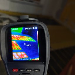 Tomasz Piecyk voltom instalacje elektryczne pomiary - Termowizja podłogówki: kamera ukazuje rozkład temperatur w ogrzewaniu podłogowym, detale na ekranie urządzenia, widoczne rury grzewcze i okno w tle.