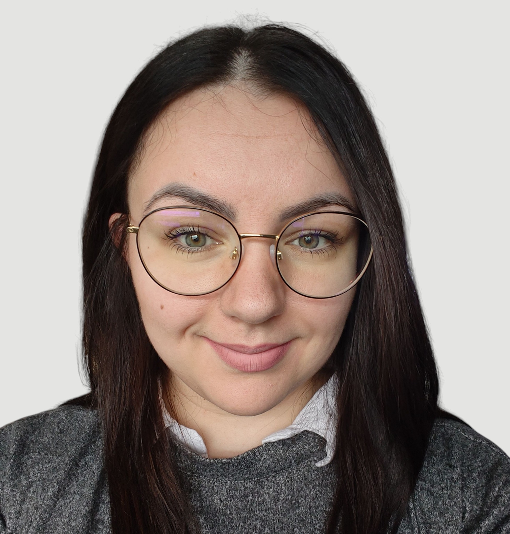 Portret uśmiechniętej brunetki w okularach o złotych oprawkach, ubrana w szary sweter i białą koszulę. Jasne tło, naturalne światło.