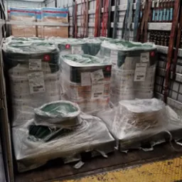 Wnętrze naczepy z załadunkiem: palety z owiniętymi folią bębnami i pudełkami, zabezpieczone pasami transportowymi wzdłuż ścian. Żółto-czarna podłoga naczepy.