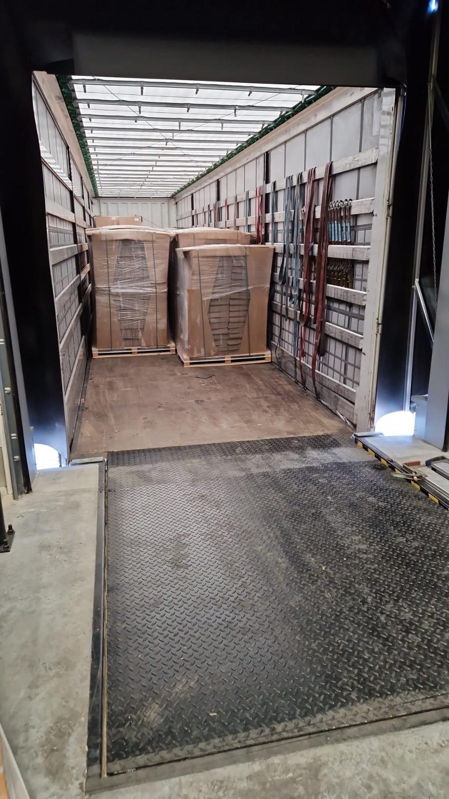 Wnętrze naczepy z załadowanymi paletami owiniętymi folią. Widoczne pasy mocujące ładunek wzdłuż ścian. Rampa załadowcza z blachą ryflowaną.