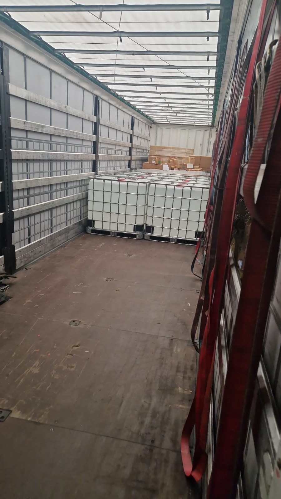 Wnętrze naczepy z ładunkiem zbiorników IBC zabezpieczonych pasami transportowymi. Widoczne elementy konstrukcyjne naczepy i podłoga z mocowaniami.
