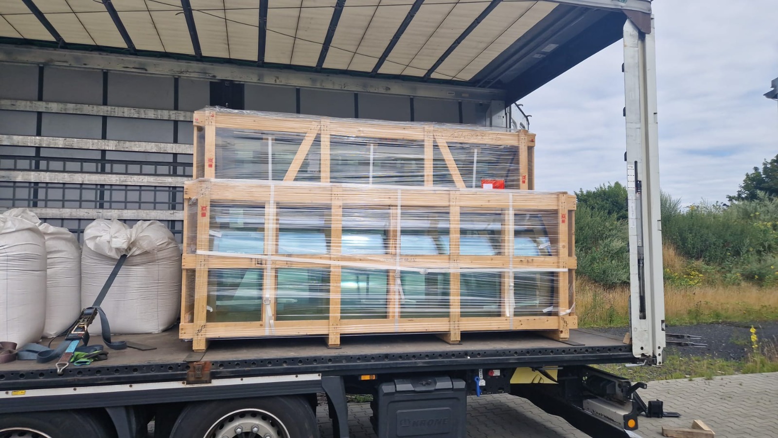 Transport okien w drewnianych skrzyniach, zabezpieczonych folią, w Radomsku. Widoczne worki z materiałem i elementy naczepy ciężarówki.