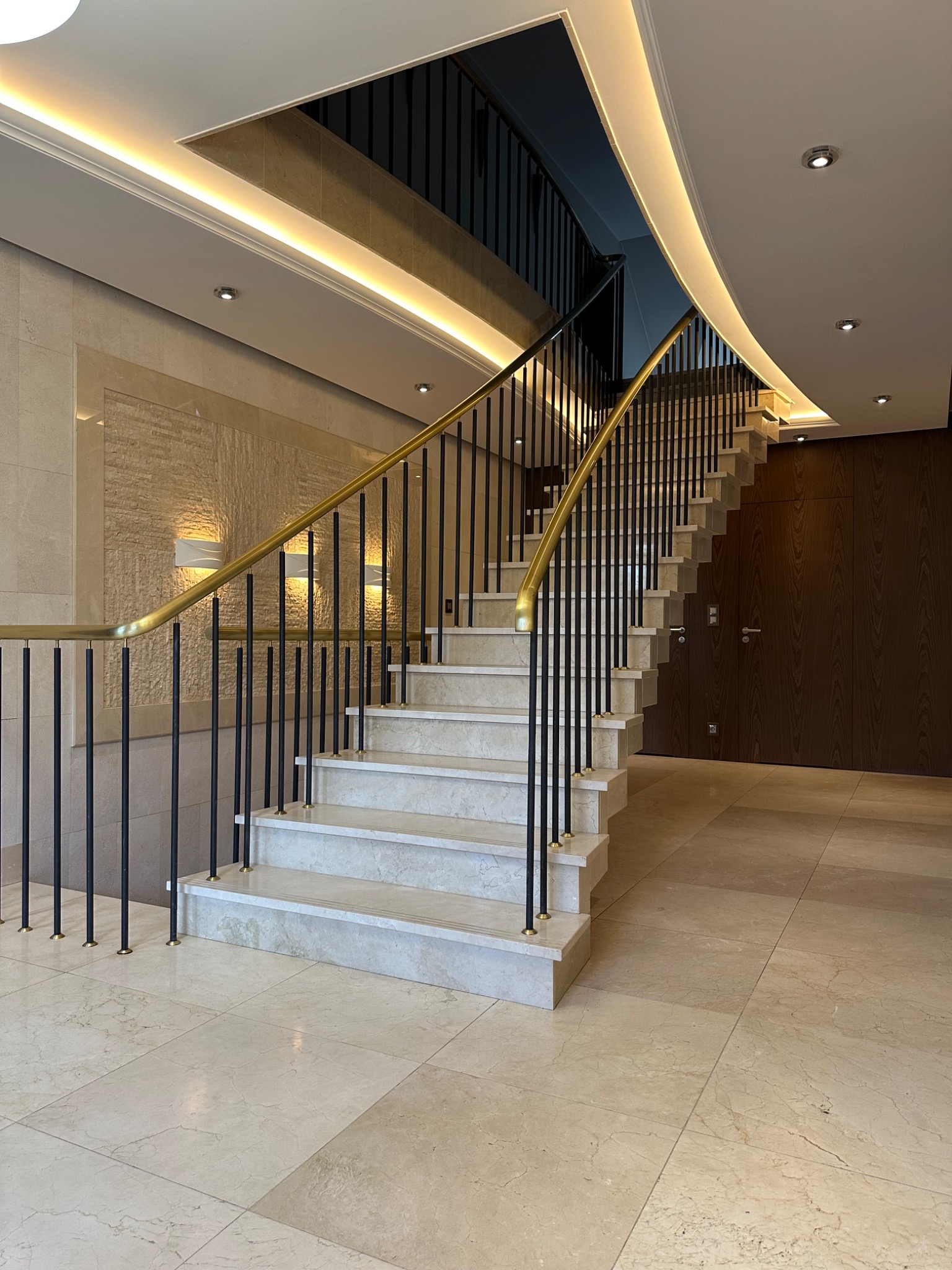 Eleganckie schody z marmurowymi stopniami i złotą balustradą w Kiekrz. Oświetlenie LED podkreśla nowoczesny design wnętrza. Widoczny fragment ściany z dekoracyjną fakturą.