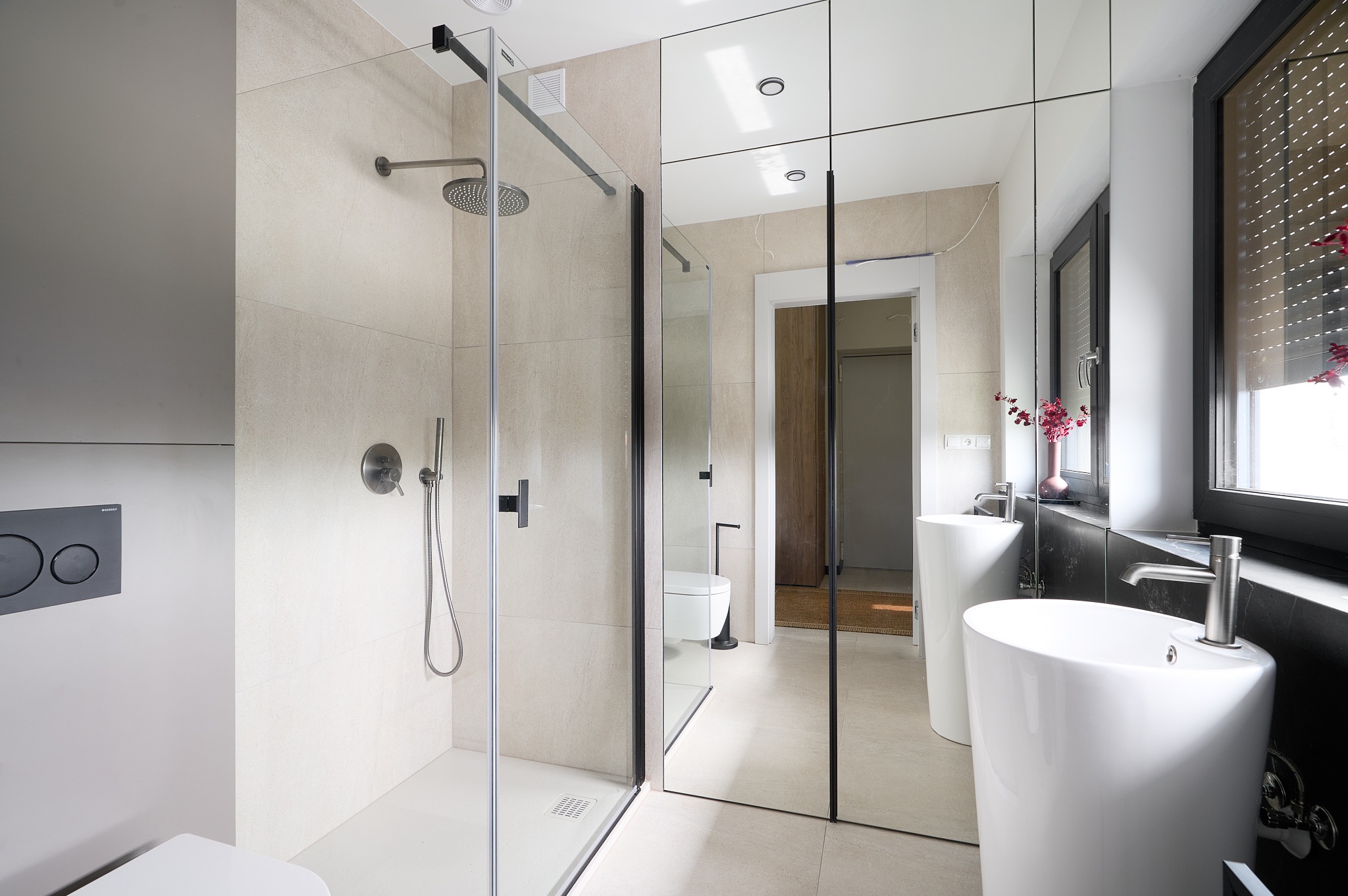 Nowoczesna łazienka z kabiną prysznicową typu walk-in, umywalkami wolnostojącymi i lustrami w czarnych ramach. Minimalistyczny design, jasne płytki i czarne akcenty.