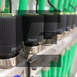 Enehouse Rafał Sołek - Rozdzielacz ogrzewania podłogowego z zielonymi rurami i czarnymi termostatami ENGO, widok z bliska na instalację. Elementy systemu grzewczego.