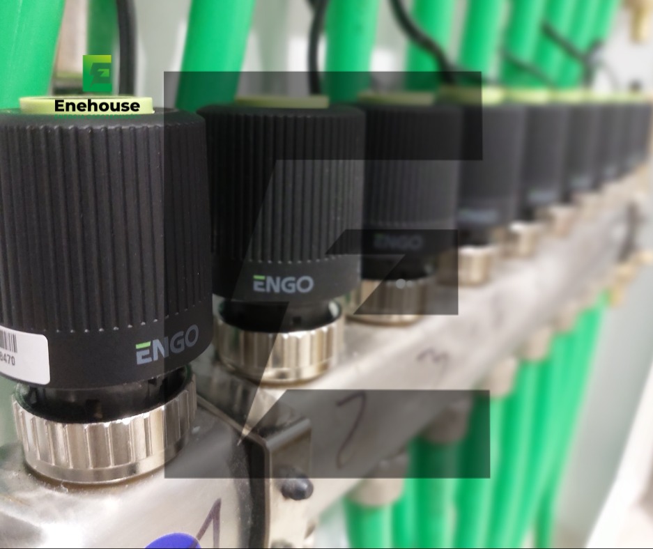 Rozdzielacz ogrzewania podłogowego z zielonymi rurami i czarnymi termostatami ENGO, widok z bliska na instalację. Elementy systemu grzewczego.