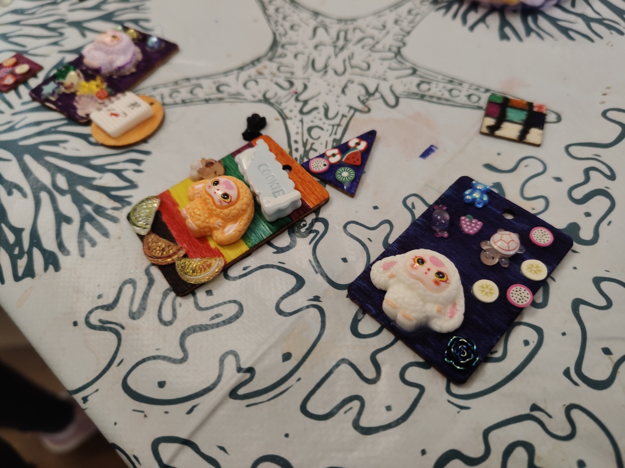 Ręcznie robione, kolorowe ozdoby z modeliny na stole z wzorem w Szczecinie. Figurki zwierząt, owoce i słodycze na drewnianych podstawkach.