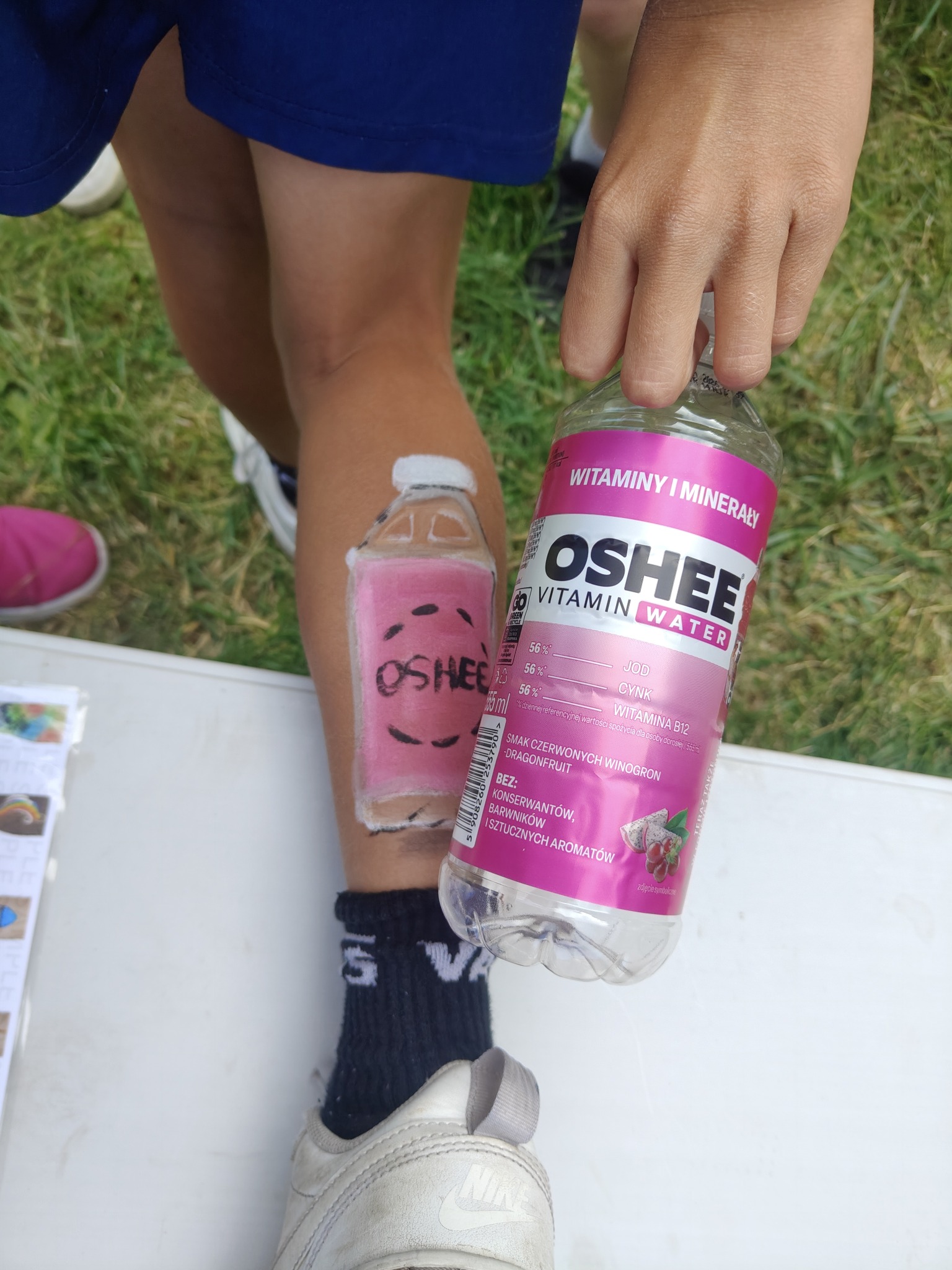 Malunek na nodze dziecka przedstawia butelkę Oshee, obok trzymana jest prawdziwa butelka tego napoju. Zabawny motyw na imprezę dla dzieci.