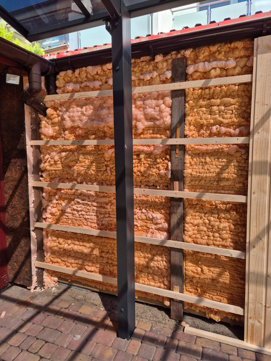 Ocieplenie ściany zewnętrznej pianą montażową, widoczne drewniane listwy konstrukcyjne. Detal z bliska, ukazujący strukturę piany i elementy mocujące.