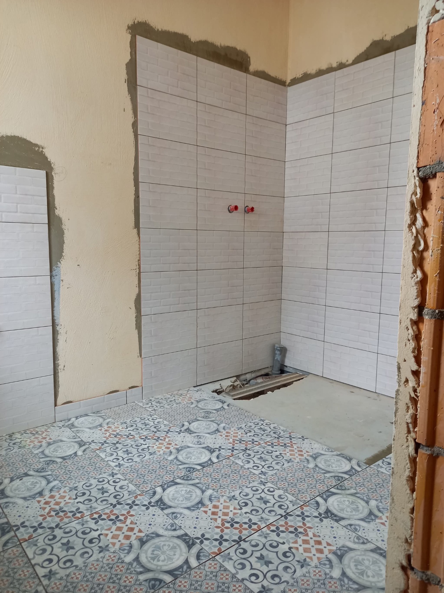 Łazienka w trakcie prac: ułożone płytki podłogowe z wzorem i białe, cegiełkowe płytki ścienne. Widoczne niedokończone fragmenty ścian i instalacji.