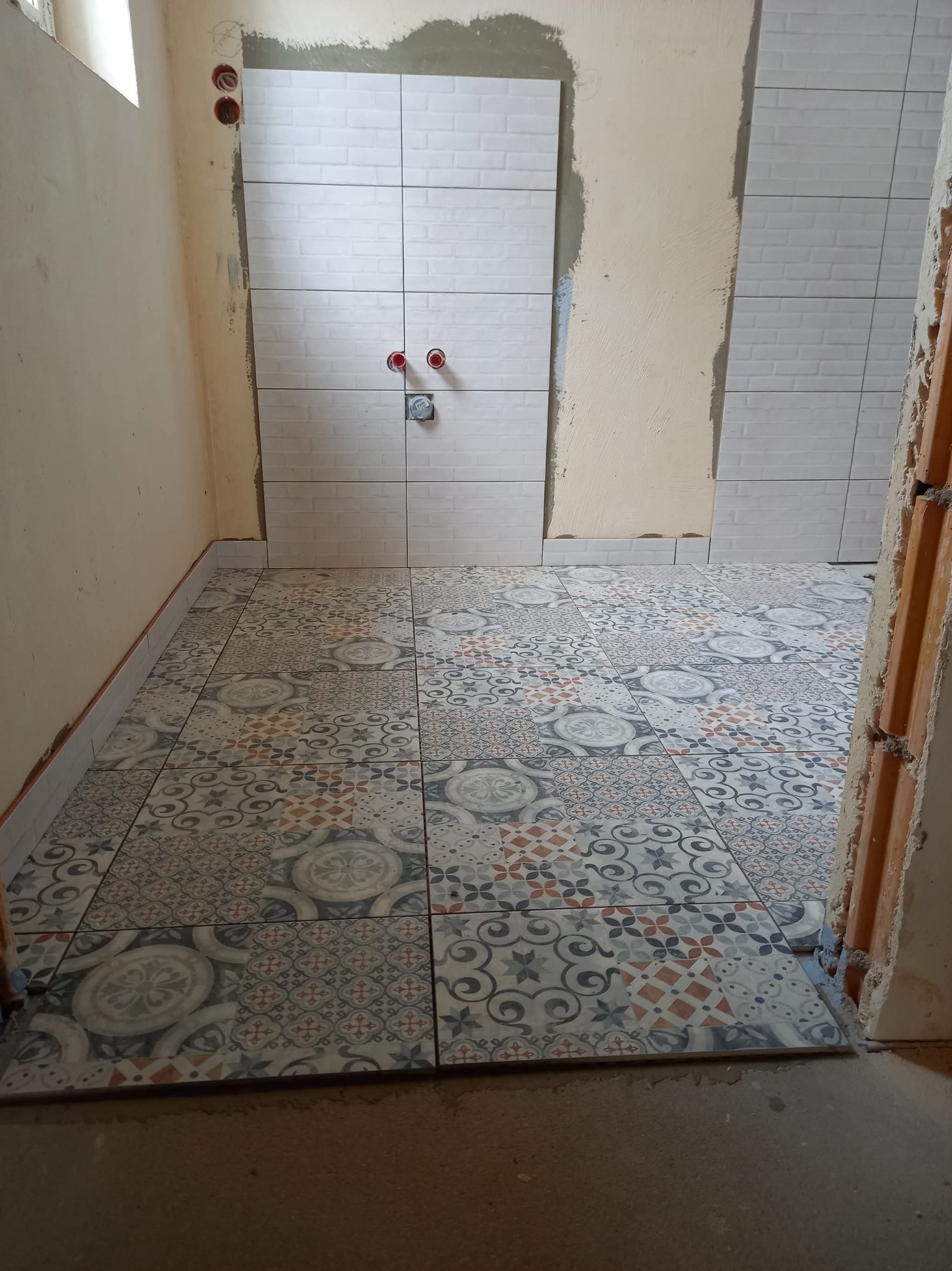 Układanie płytek podłogowych i ściennych w łazience w Murowanej Goślinie. Widoczne wzorzyste płytki na podłodze i białe płytki imitujące cegłę na ścianie.