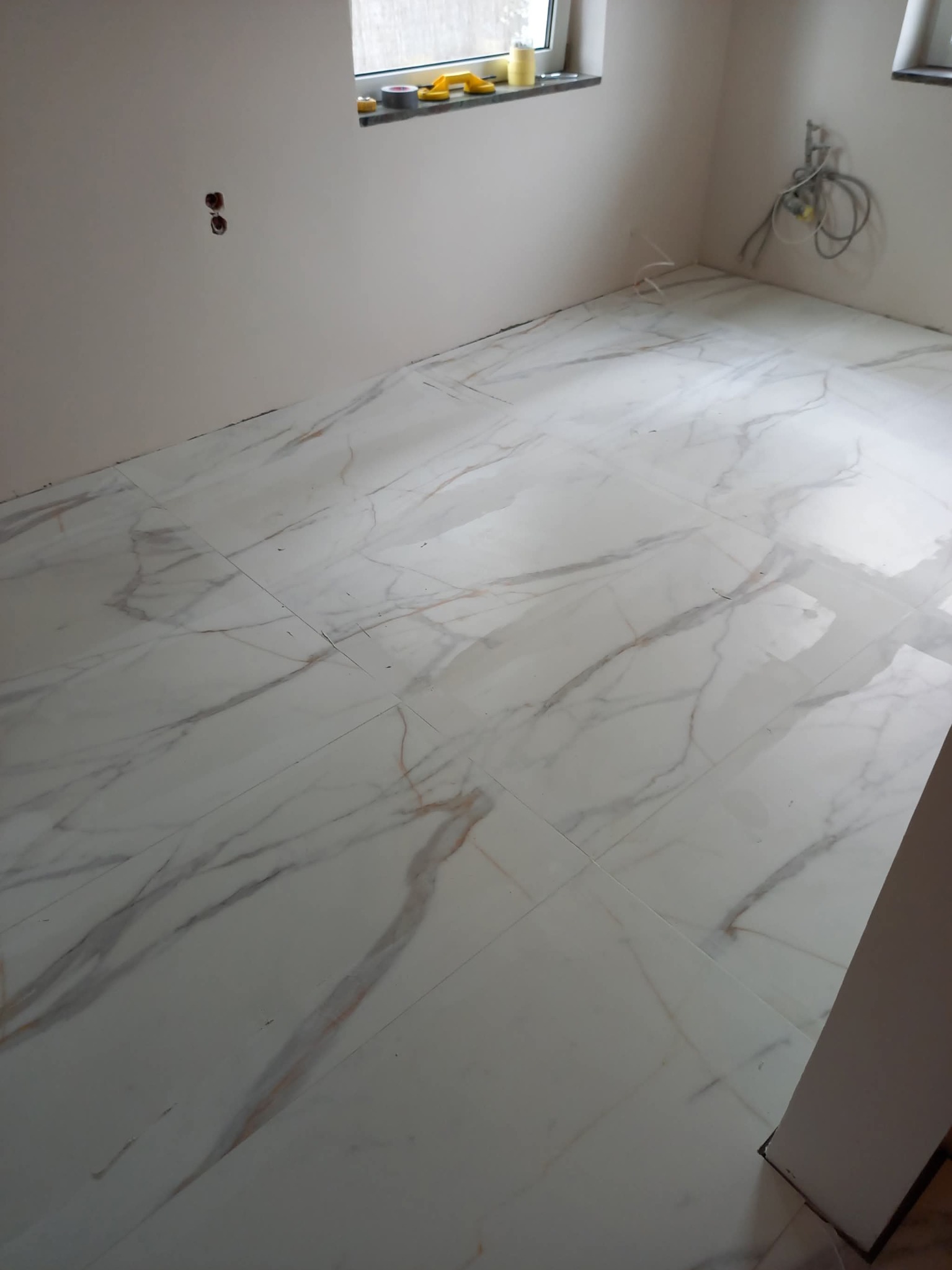 Białe płytki podłogowe z marmurkowym wzorem w jasnym pomieszczeniu z oknem i wystającymi kablami. Widok z góry, ukończona podłoga.
