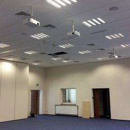 NEXA ENERGY Leszek Korycki - Sufit biura z równomiernie rozmieszczonymi lampami i projektorami, niebieska wykładzina podłogowa, białe ściany i składane ścianki działowe.