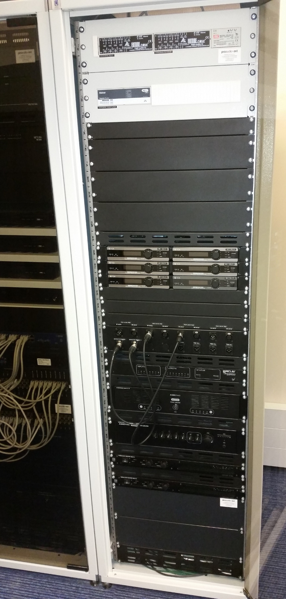 Profesjonalna szafa rack z zainstalowanym sprzętem audio-wideo, widoczne kable i urządzenia różnych producentów, gotowa do pracy.