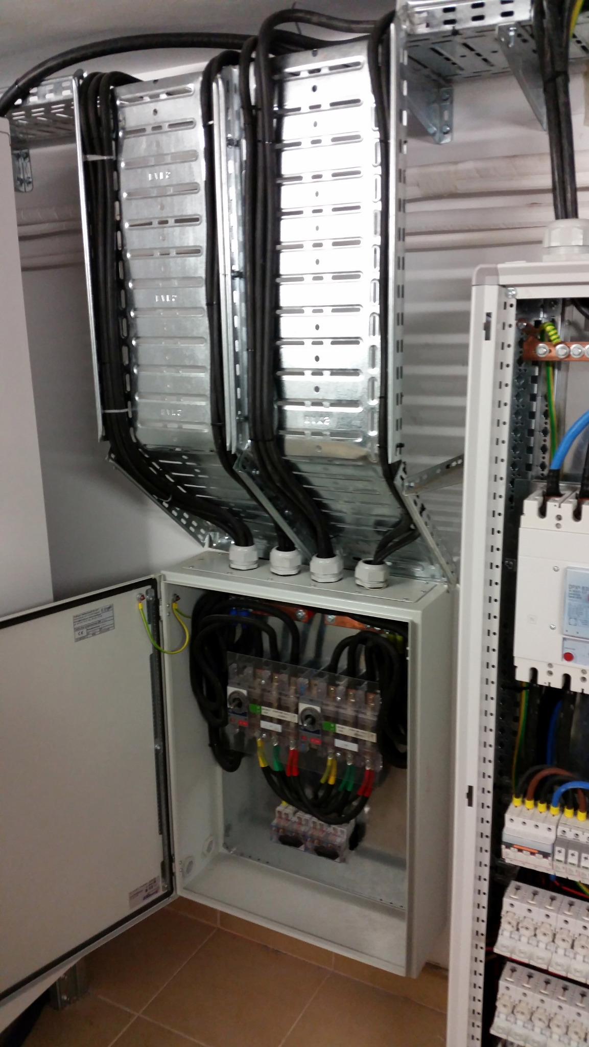 Rozdzielnia elektryczna z otwartymi drzwiami, widoczne kable w metalowych korytkach i zabezpieczenia. Profesjonalny montaż instalacji elektrycznej w budynku.