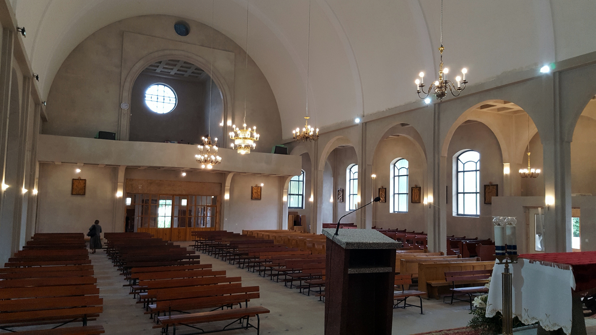 Wnętrze kościoła w Garwolinie z ławkami, oświetleniem i amboną. Widoczne okna łukowe i żyrandole. Oświetlenie punktowe na ścianach.