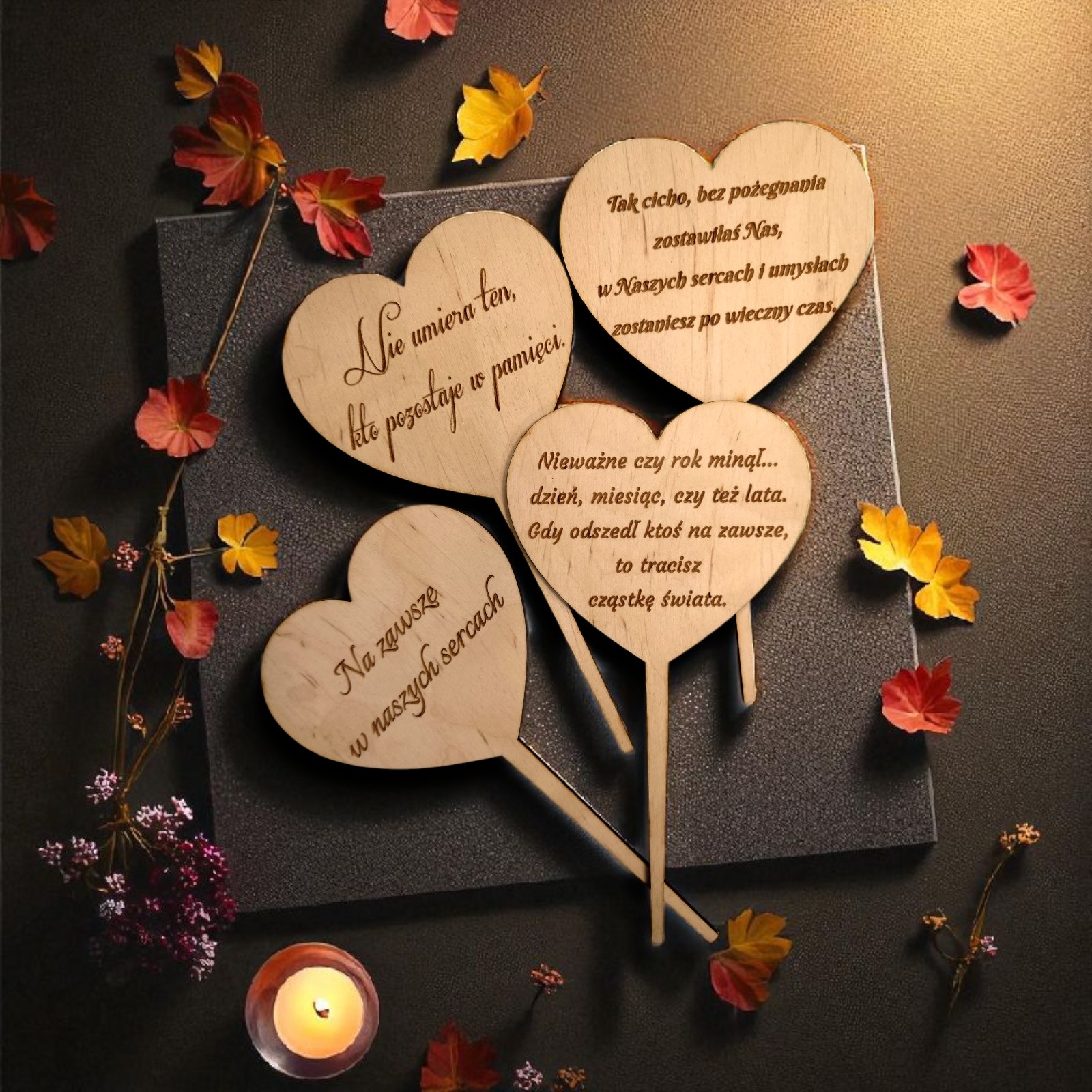 Drewniane serca z grawerem pamiątkowych sentencji, otoczone jesiennymi liśćmi i świecą, na ciemnym tle. Upominek introligatorski z personalizacją.