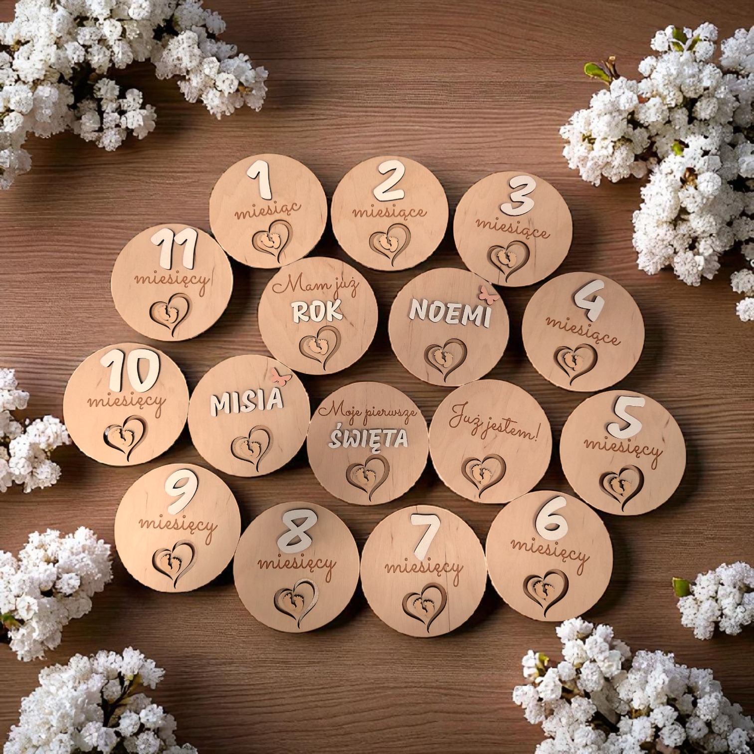 Drewniane krążki z wygrawerowanymi napisami, oznaczające kolejne miesiące życia dziecka, ułożone na drewnianym stole, otoczone białymi kwiatami. Unikalny zestaw do sesji zdjęciowych.