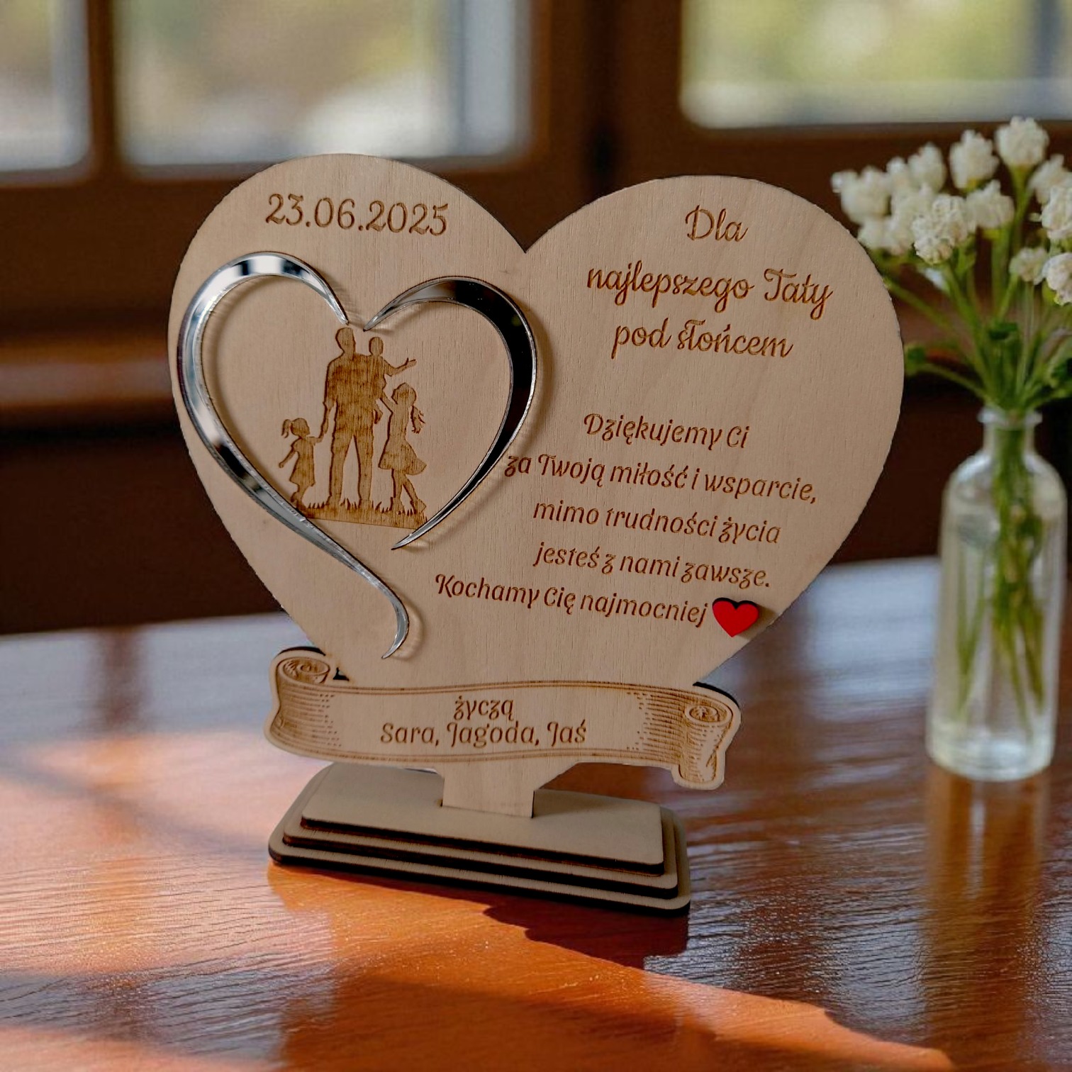 Drewniana statuetka w kształcie serca z wygrawerowanym napisem 'Dla najlepszego Taty pod słońcem' i datą 23.06.2025, stojąca na drewnianej podstawie.