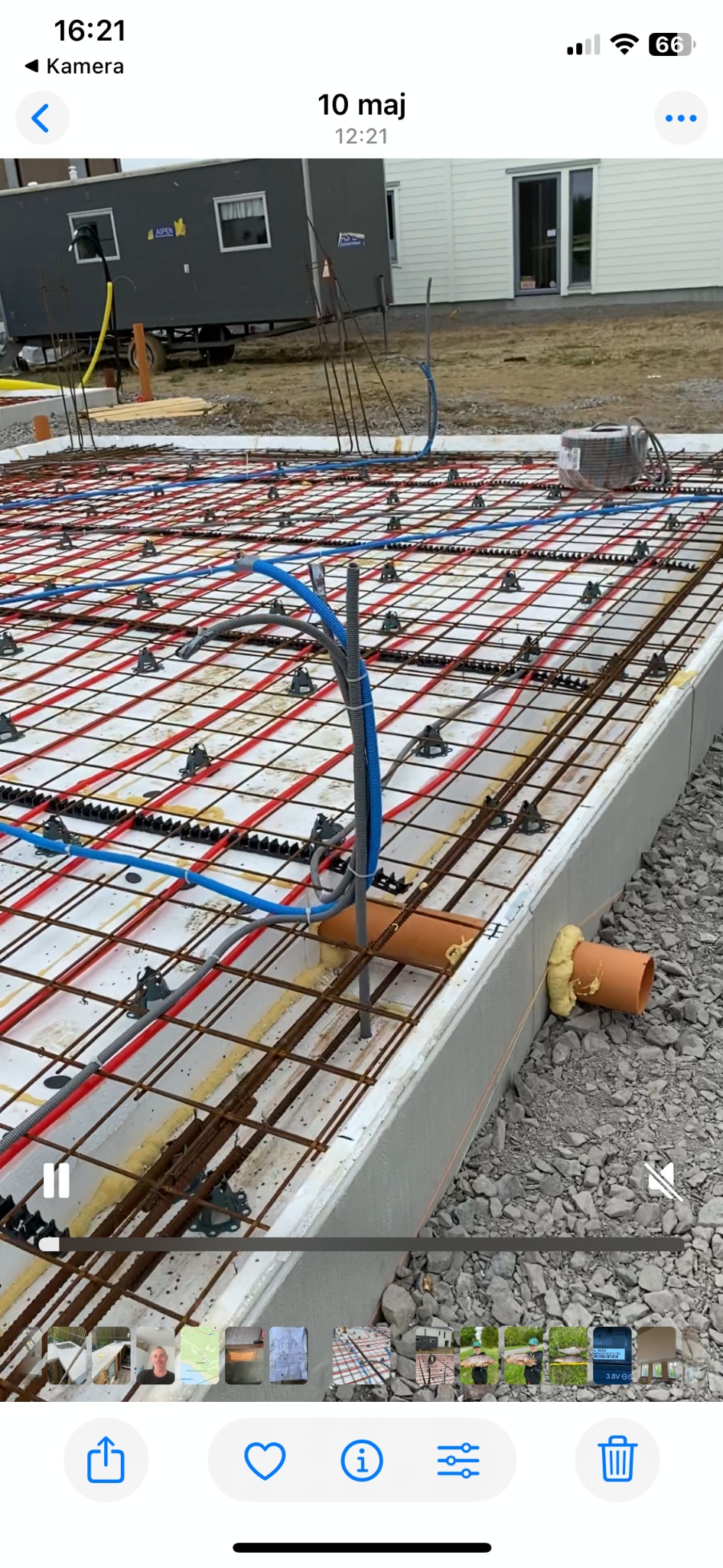 Fundament budynku z rozłożoną instalacją ogrzewania podłogowego, widoczne rury grzewcze i zbrojenie. Na zewnątrz budynku stoi przyczepa budowlana.