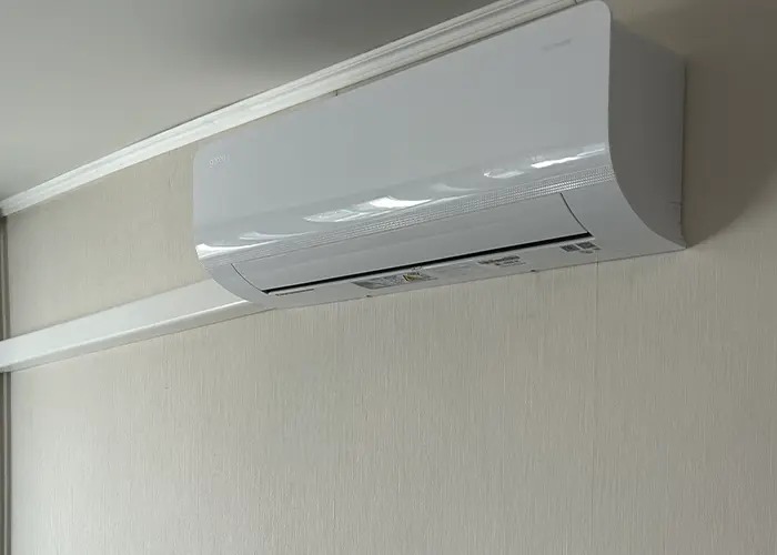 Biała jednostka wewnętrzna klimatyzacji zamontowana na jasnej ścianie z delikatną fakturą, widoczna listwa przypodłogowa. Ujęcie z bliska, bez dodatkowych elementów dekoracyjnych.