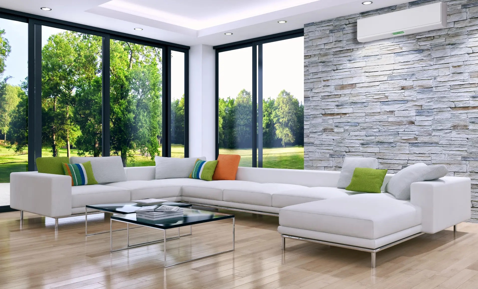 Nowoczesny salon z klimatyzacją: biała sofa narożna, kamienna ściana, duże okna z widokiem na zieleń. Klimatyzator dyskretnie zamontowany nad ścianą.