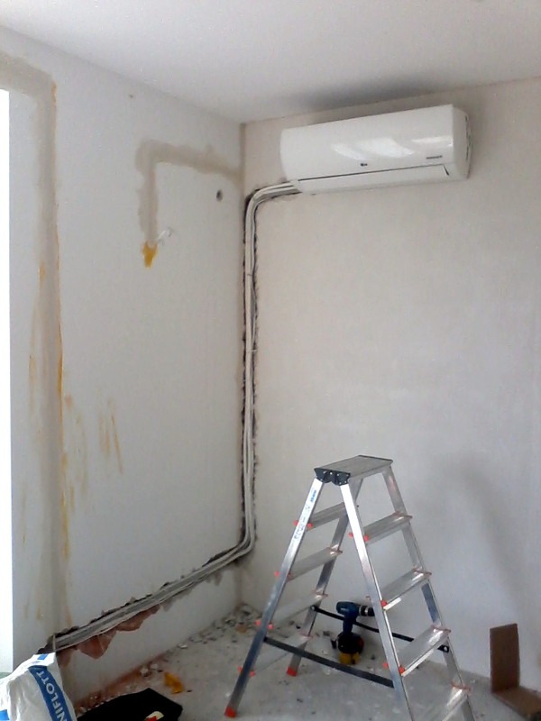 Montaż klimatyzacji w rogu pokoju: biała jednostka na ścianie, kable w listwach, drabina aluminiowa, ślady po pracach wykończeniowych na ścianach.