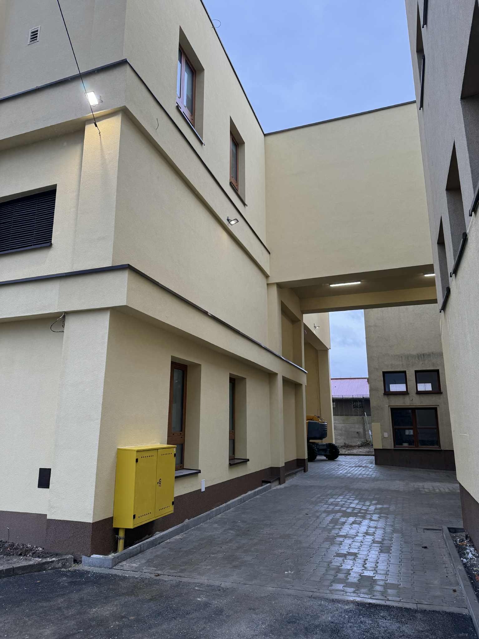 Elewacja budynku po remoncie, kremowe ściany, brązowe okna, żółta skrzynka gazowa, kostka brukowa na chodniku. Widok z dołu, perspektywa uliczna.