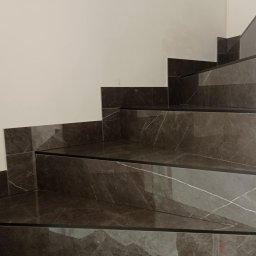 maksym boichuk - Schody wykończone ciemnym gresem imitującym marmur z wyraźnym żyłowaniem, widoczne z bliska, z czarnymi listwami wykończeniowymi. Minimalistyczne wnętrze.