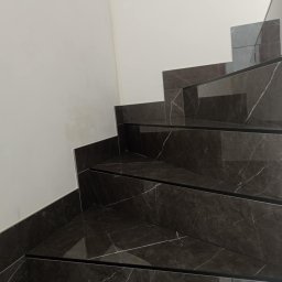 maksym boichuk - Wykończone schody z ciemnego marmuru z białymi żyłami, elegancko wkomponowane w jasne wnętrze. Widoczne detale wykończenia i precyzja ułożenia płytek.