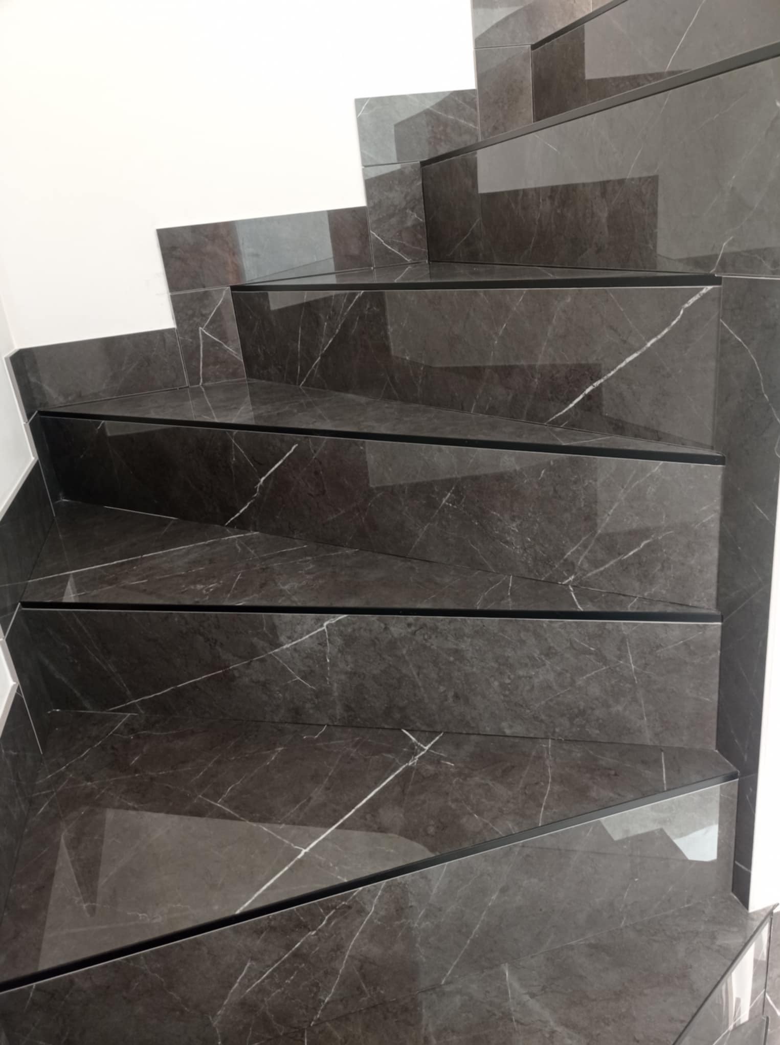 Schody wykończone ciemnym gresem imitującym marmur z białymi żyłami, widok z góry, precyzyjne ułożenie płytek, minimalistyczne wykończenie.
