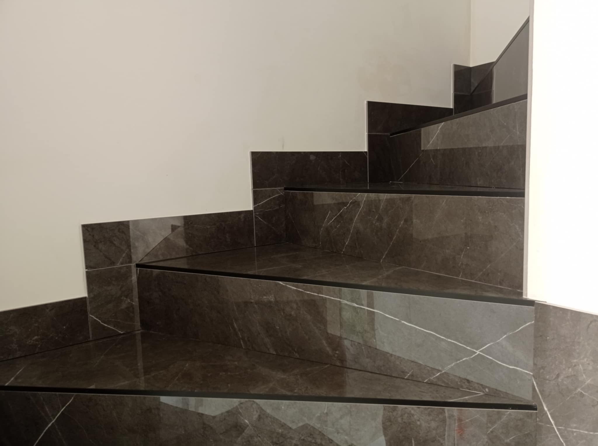 Schody wykończone ciemnym gresem imitującym marmur z wyraźnym żyłowaniem, widoczne z bliska, z czarnymi listwami wykończeniowymi. Minimalistyczne wnętrze.