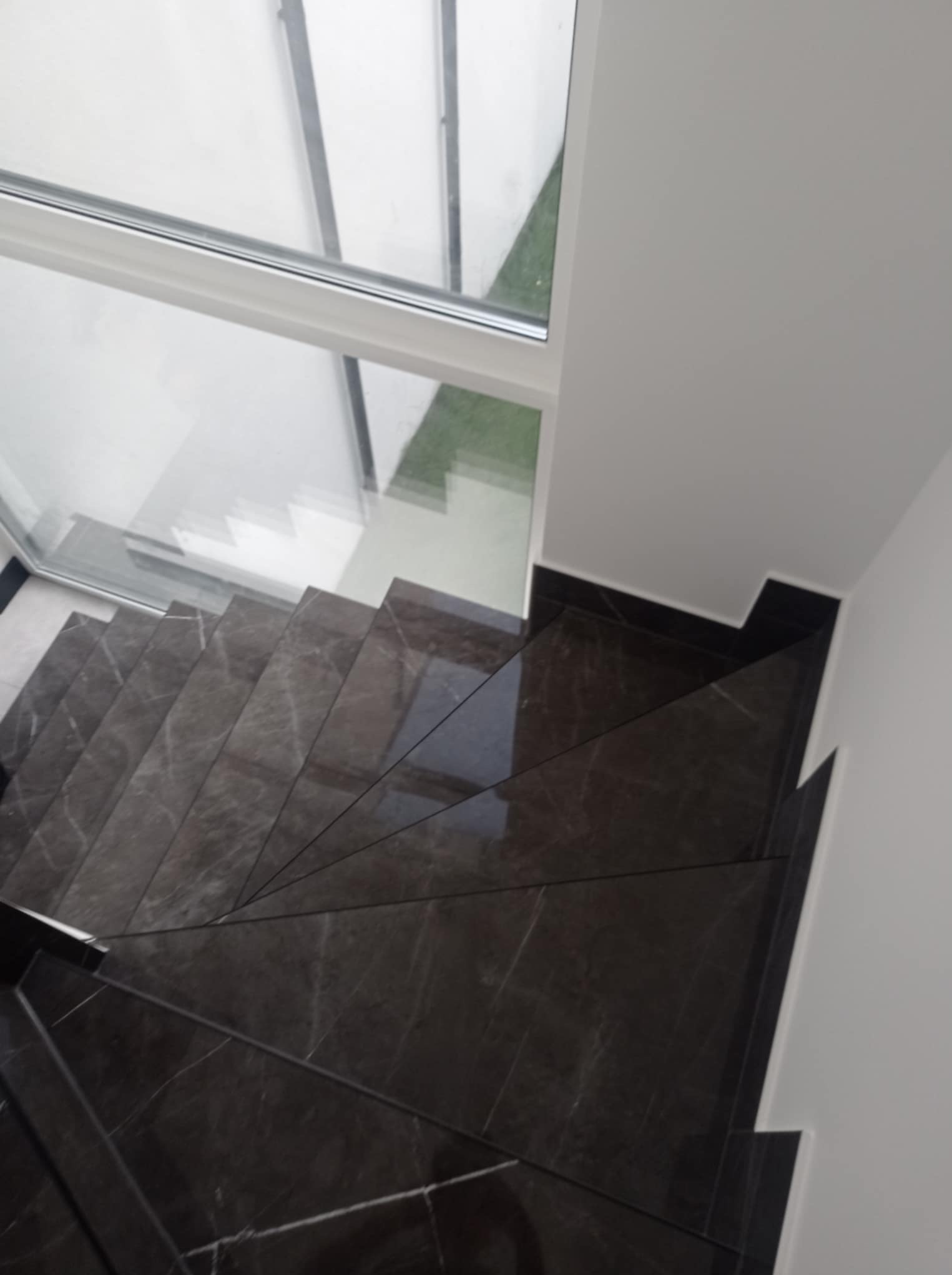 Schody wyłożone ciemnym marmurem z białymi żyłkami, widok z góry, z oknem w tle. Minimalistyczny design, precyzyjne wykończenie, nowoczesne wnętrze.