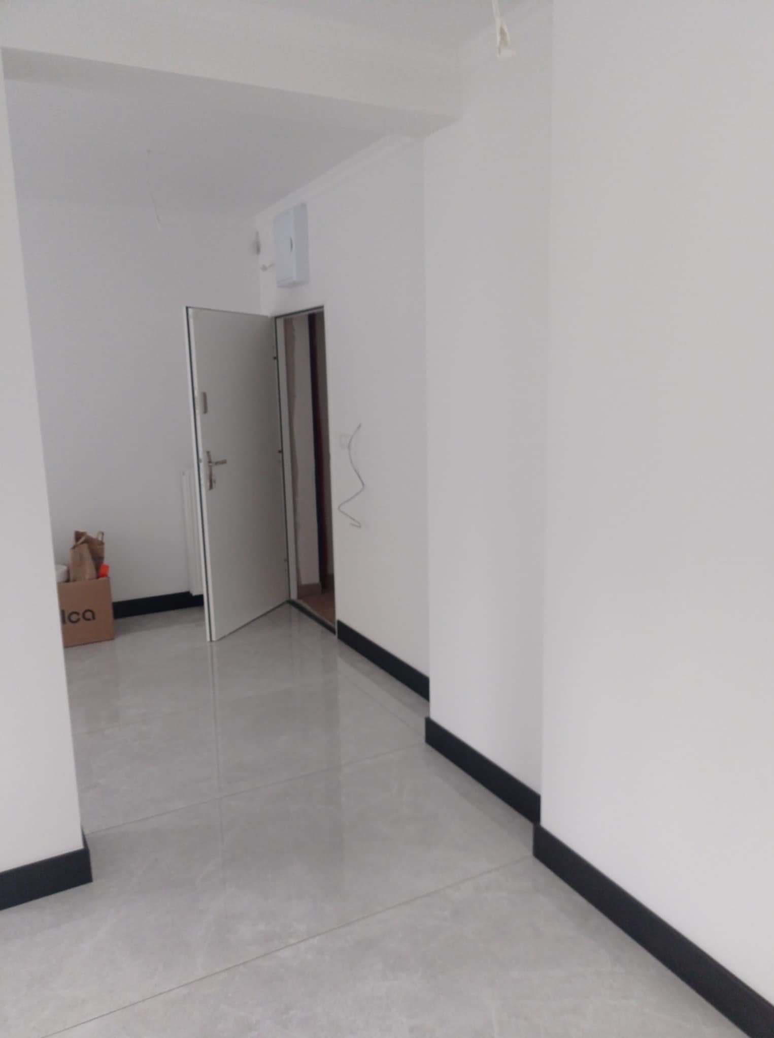Wnętrze po remoncie: białe ściany z czarnymi listwami przypodłogowymi, szara podłoga z połyskiem, otwarte drzwi. Widoczny karton z napisem 'Ica'.