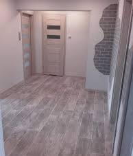 Jasne wnętrze po remoncie: drewnopodobna podłoga, białe ściany z dekoracyjnym motywem cegły, drzwi wewnętrzne z poziomymi przeszkleniami i ościeżnica w minimalistycznym stylu.