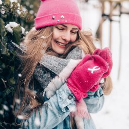 Magoń Fotografia i Film Dominik Magoń - Uśmiechnięta blondynka w różowej czapce i rękawiczkach pozuje w zimowej scenerii w Gnieznie. Śnieg pada, a ona otulona jest szalem i dżinsową kurtką.