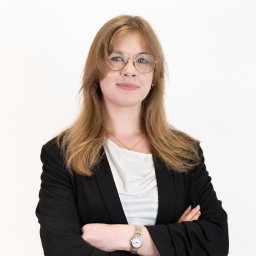 Magoń Fotografia i Film Dominik Magoń - Portret kobiety w okularach, ubrana w czarną marynarkę i białą bluzkę, z założonymi rękami. Jasne tło, naturalne światło, widoczny zegarek na ręce.