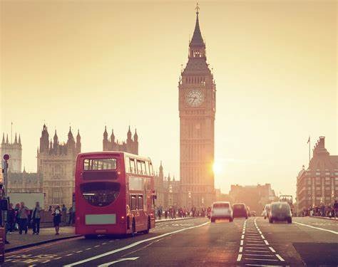 Londyn w słonecznym świetle: czerwony autobus na tle Big Bena i Parlamentu. Dynamiczne ujęcie z perspektywy jezdni, w tle sylwetki przechodniów i budynki.