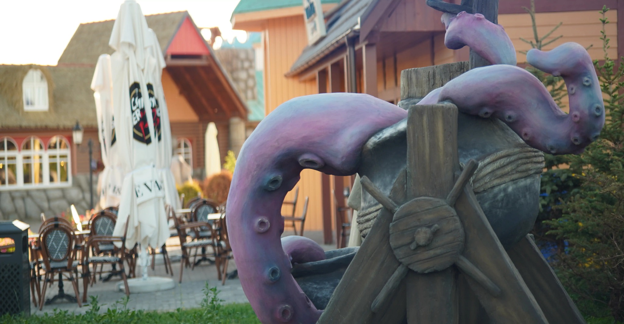 Dekoracyjna rzeźba ośmiornicy na tle budynku z parasolami i stolikami, tworząca unikalny wystrój zewnętrzny.