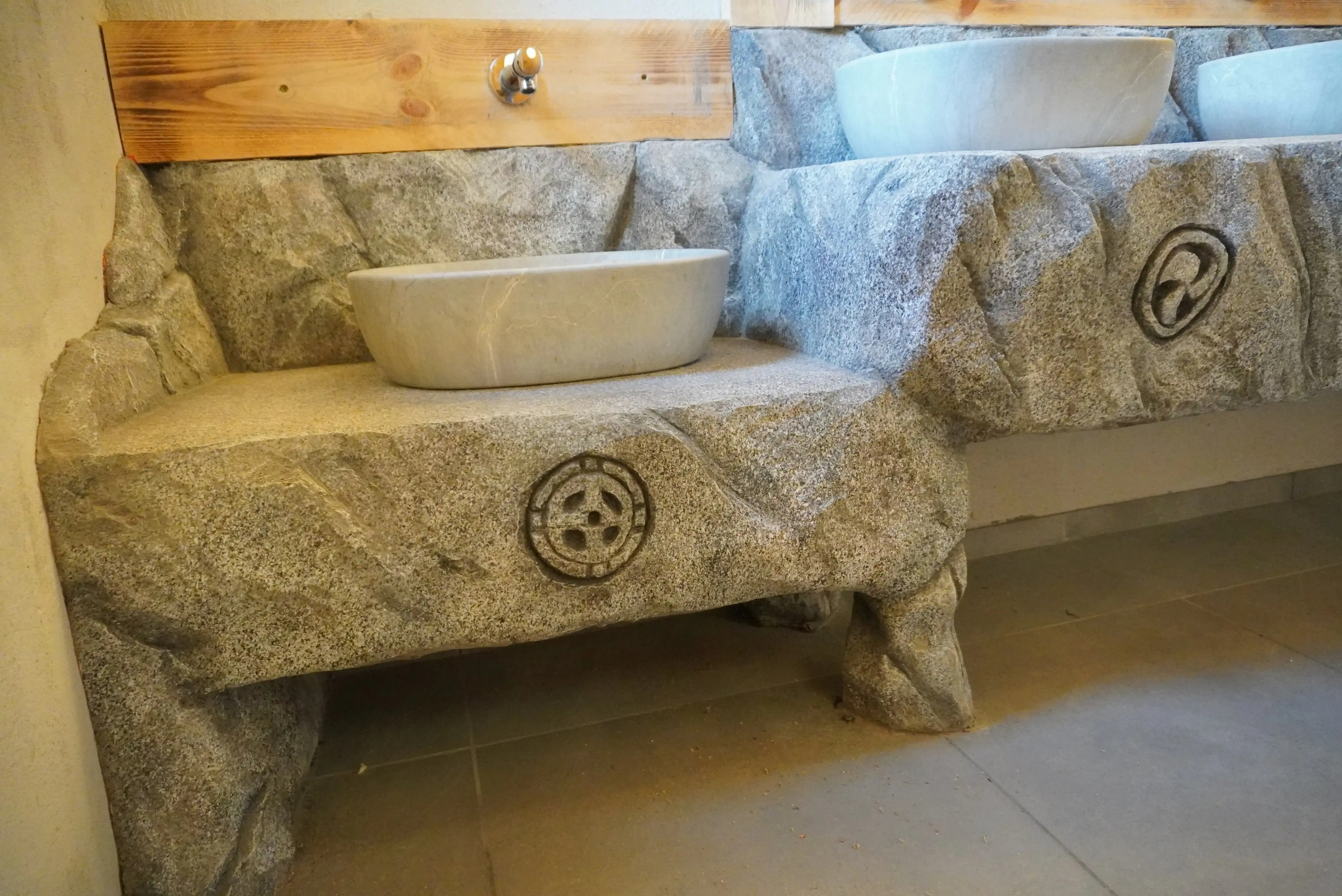 Kamienna umywalka z rzeźbionym wzorem w łazience. Naturalne materiały i unikalny design. Wykończenie wnętrza z kamienia.