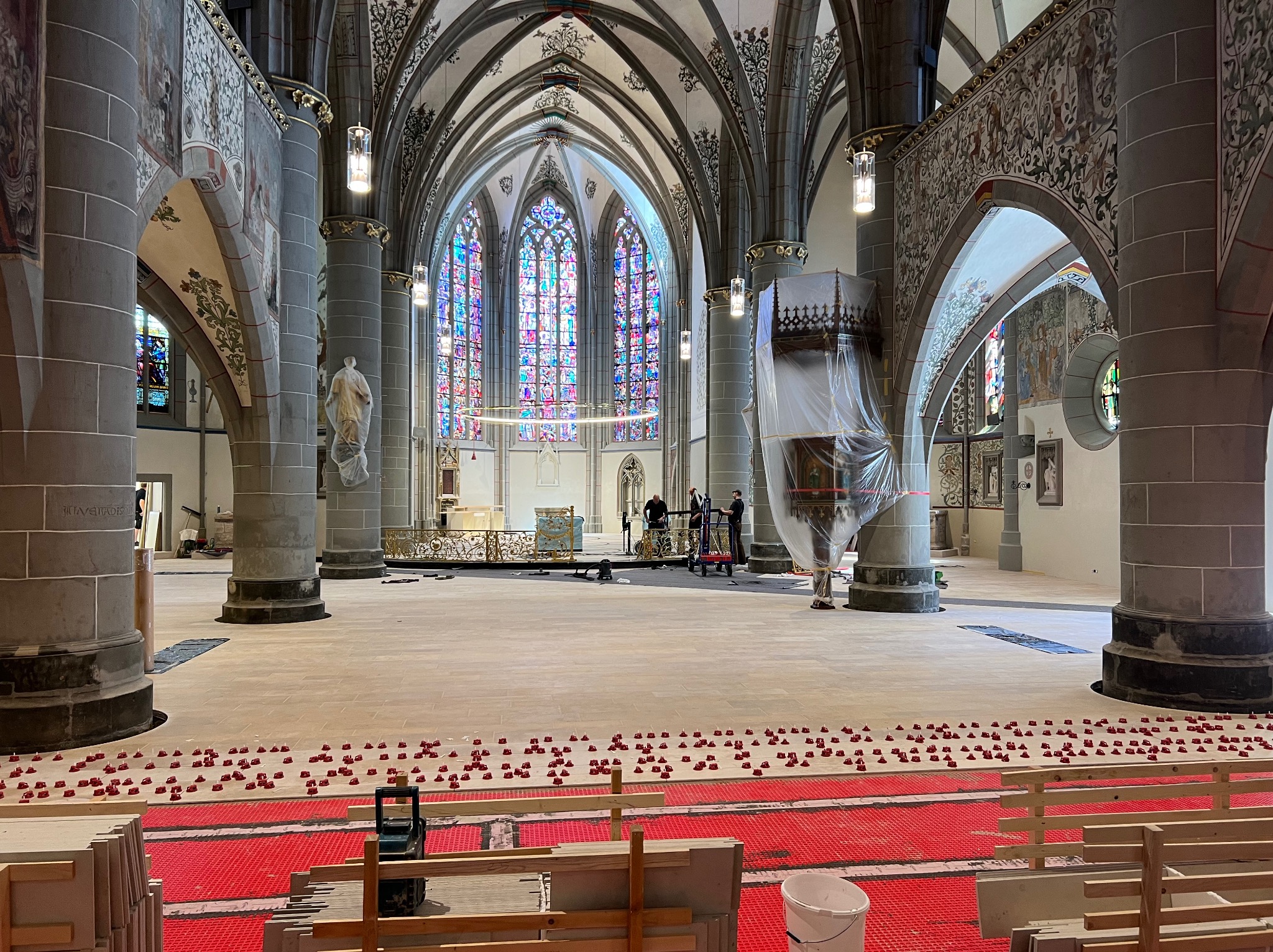 Wnętrze kościoła w trakcie remontu posadzki: czerwona mata grzewcza, poziomowanie pod płytki, kolumny, witraże. Prace wykończeniowe w zabytkowym obiekcie sakralnym.