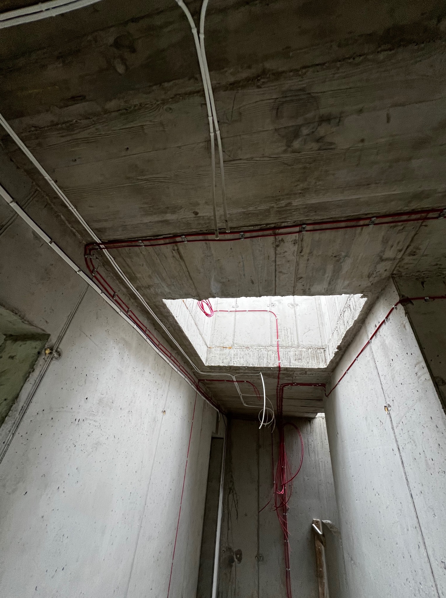 Surowy beton i czerwone kable elektryczne zamocowane na ścianach i suficie wewnątrz budynku w trakcie budowy. Widok z dołu na sufit z otworem.