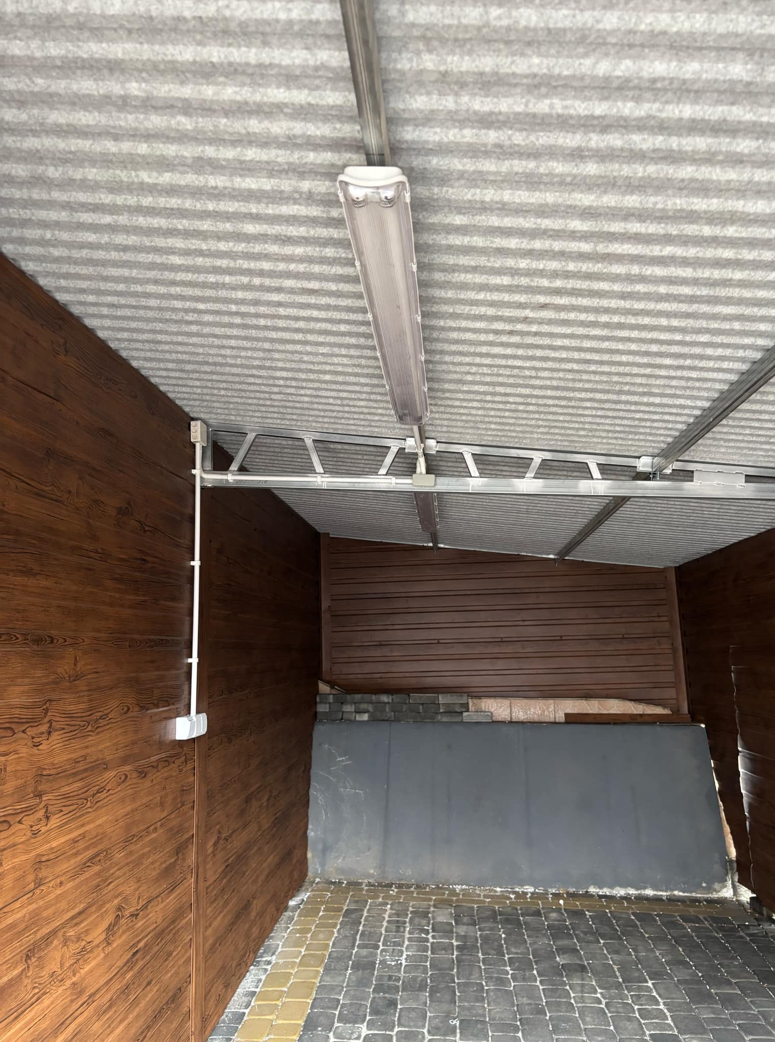 Wnętrze zadaszenia z drewnianą boazerią, oświetlone pojedynczą lampą jarzeniową. Widoczne przewody elektryczne w listwach na ścianie.